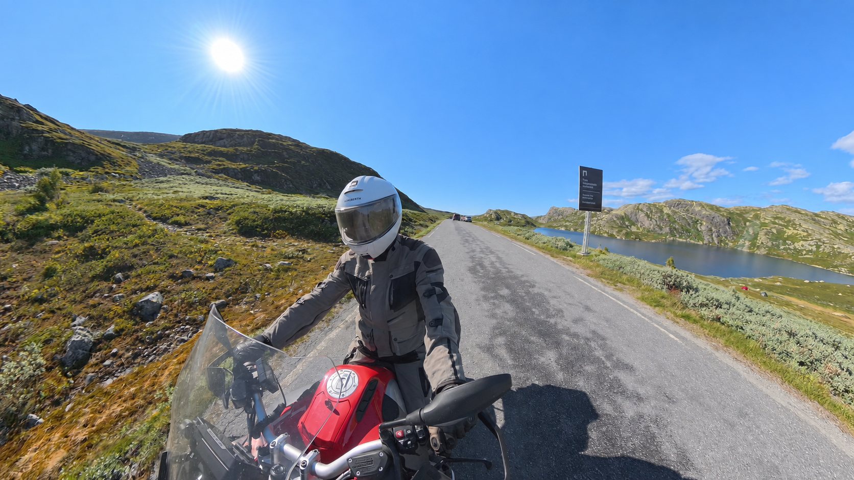 Motorsykkeltur på en asfaltvei gjennom norsk fjellandskap, med fjellvann langs veien